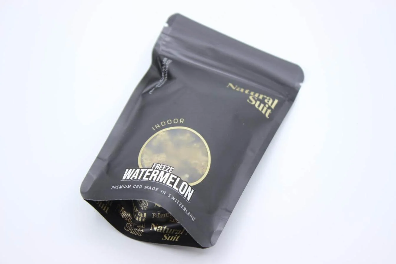 Bodegón aéreo de envase kraft Natural Suit con cogollos CBD, cerámica neutra y props lifestyle