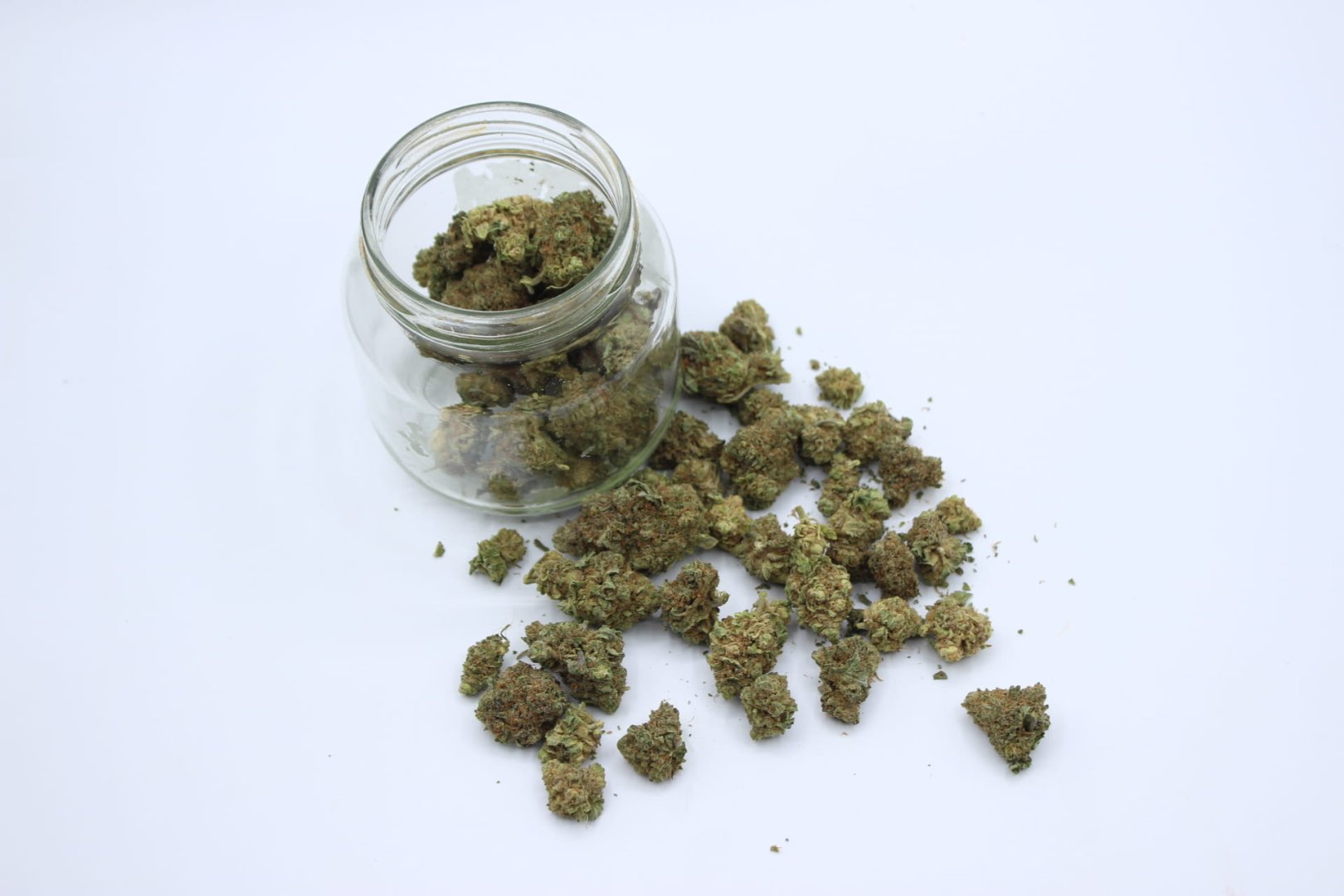 Tarro de cristal abierto con flores de CBD premium esparcidas alrededor