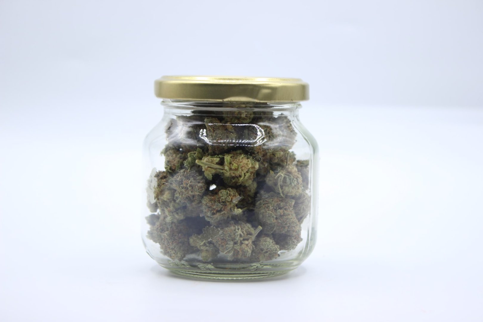 Tarro de cristal con tapa dorada lleno de flores de CBD premium